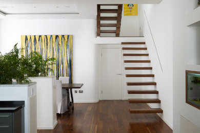 Medium sized contemporary wood l-shaped glass railing staircase in London with open risers and feature lighting.
