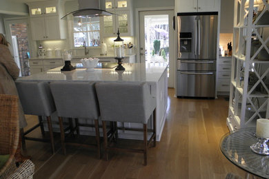 Inspiration for a mid-sized transitional galley light wood floor and brown floor eat-in kitchen remodel in Atlanta with an undermount sink, shaker cabinets, white cabinets, quartz countertops, white backsplash, ceramic backsplash, stainless steel appliances and an island