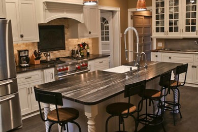 Mid-sized transitional l-shaped dark wood floor and brown floor open concept kitchen photo in Philadelphia with a farmhouse sink, shaker cabinets, white cabinets, soapstone countertops, beige backsplash, stone tile backsplash, stainless steel appliances and an island