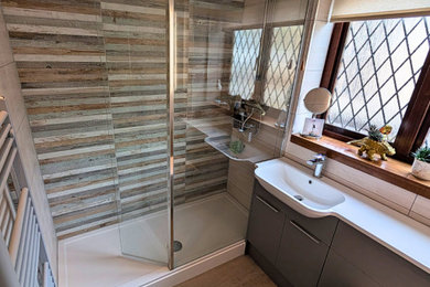 Inspiration for a medium sized modern family bathroom in West Midlands with flat-panel cabinets, grey cabinets, a walk-in shower, a one-piece toilet, multi-coloured tiles, porcelain tiles, laminate floors, an integrated sink, solid surface worktops, brown floors, an open shower, white worktops, a single sink and a built in vanity unit.