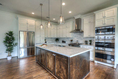 Inspiration for a transitional l-shaped medium tone wood floor open concept kitchen remodel in Houston with a double-bowl sink, shaker cabinets, white cabinets, marble countertops, gray backsplash, marble backsplash, stainless steel appliances, an island and white countertops