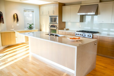 This is an example of a mid-sized contemporary l-shaped open plan kitchen in Vancouver with an undermount sink, flat-panel cabinets, light wood cabinets, quartz benchtops, stainless steel appliances, light hardwood floors, with island and grey splashback.