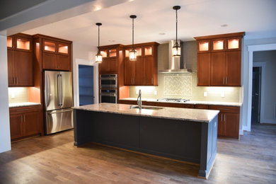 Inspiration for a large craftsman galley medium tone wood floor and brown floor eat-in kitchen remodel in Raleigh with a drop-in sink, shaker cabinets, medium tone wood cabinets, granite countertops, green backsplash, glass tile backsplash, stainless steel appliances, an island and multicolored countertops