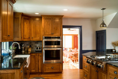 Kitchen - mid-sized country medium tone wood floor and brown floor kitchen idea in Other with a farmhouse sink, recessed-panel cabinets, medium tone wood cabinets, granite countertops, gray backsplash, stainless steel appliances and gray countertops
