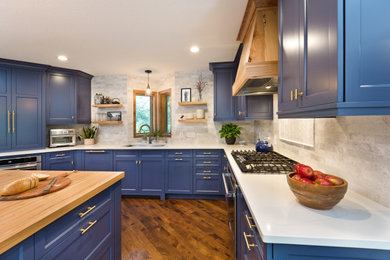 Mid-sized trendy u-shaped medium tone wood floor and brown floor open concept kitchen photo in San Francisco with a double-bowl sink, shaker cabinets, blue cabinets, quartz countertops, beige backsplash, stone tile backsplash, stainless steel appliances, an island and white countertops