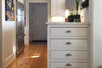 Mid-sized transitional l-shaped light wood floor enclosed kitchen photo in Burlington with shaker cabinets, white cabinets, marble countertops, white backsplash, stone slab backsplash, stainless steel appliances, an undermount sink and a peninsula