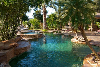 Design ideas for a large tropical backyard custom-shaped pool in Orlando with a hot tub and natural stone pavers.