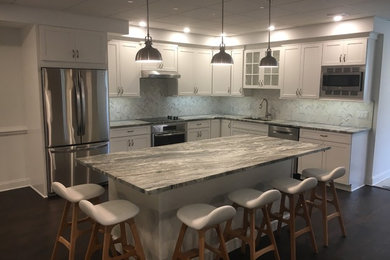 Photo of a mid-sized contemporary l-shaped kitchen in New York with an undermount sink, white cabinets, granite benchtops, ceramic splashback, stainless steel appliances, vinyl floors, with island and brown floor.