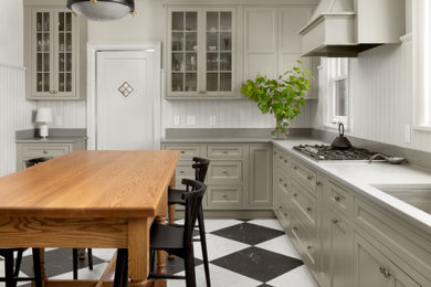 ミルウォーキーにある中くらいなトランジショナルスタイルのおしゃれなアイランドキッチン (シェーカースタイル扉のキャビネット、クオーツストーンカウンター、グレーのキッチンパネル、木材のキッチンパネル、磁器タイルの床、黒い床、グレーのキッチンカウンター) の写真