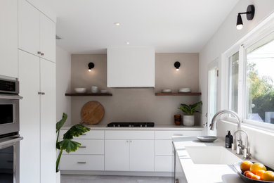 This is an example of a mid-sized contemporary galley separate kitchen in Los Angeles with a single-bowl sink, flat-panel cabinets, white cabinets, quartz benchtops, brown splashback, stainless steel appliances, cement tiles, no island, grey floor and grey benchtop.