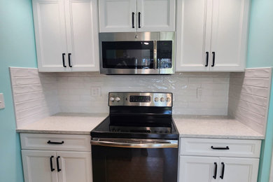 Example of a mid-sized trendy u-shaped enclosed kitchen design in Other with an undermount sink, recessed-panel cabinets, white cabinets, quartz countertops, white backsplash, ceramic backsplash, black appliances and white countertops