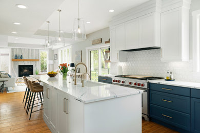 Example of a large transitional galley medium tone wood floor and tray ceiling open concept kitchen design in Minneapolis with an undermount sink, recessed-panel cabinets, blue cabinets, quartz countertops, white backsplash, ceramic backsplash, stainless steel appliances, an island and white countertops