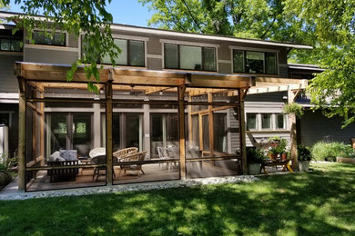 This is an example of a mid-sized transitional screened-in and wood railing back porch design in Kansas City with a pergola.