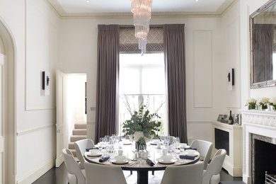 This is an example of a traditional dining room in London with white walls, dark hardwood floors, a standard fireplace and a stone fireplace surround.
