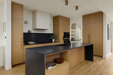 Example of a large trendy galley light wood floor kitchen pantry design in Vancouver with light wood cabinets, black backsplash, an island and black countertops
