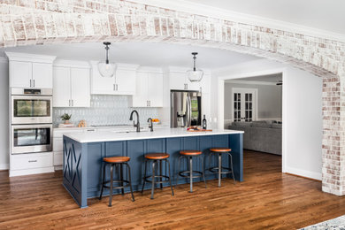 Inspiration for a large transitional l-shaped medium tone wood floor and brown floor open concept kitchen remodel in Charlotte with blue cabinets, quartz countertops, multicolored backsplash, stainless steel appliances, an island, white countertops, an undermount sink, shaker cabinets and ceramic backsplash