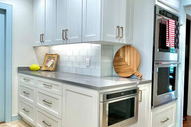 Inspiration for a large l-shaped travertine floor and beige floor open concept kitchen remodel in Oklahoma City with an undermount sink, shaker cabinets, white cabinets, quartz countertops, gray backsplash, glass tile backsplash and stainless steel appliances