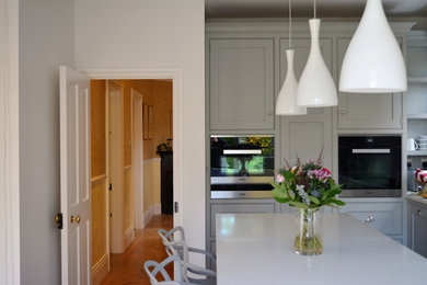 Design ideas for a large contemporary galley kitchen/diner in London with louvered cabinets, grey cabinets, marble worktops, white splashback, an island, a submerged sink, cement tile splashback, coloured appliances and laminate floors.