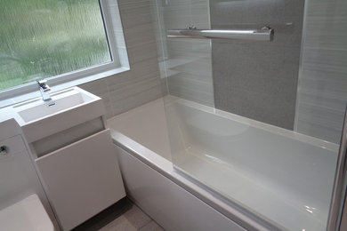 Photo of a small modern kids bathroom in West Midlands with flat-panel cabinets, white cabinets, an alcove tub, a one-piece toilet, gray tile, ceramic tile, grey walls, an integrated sink, engineered quartz benchtops and grey floor.