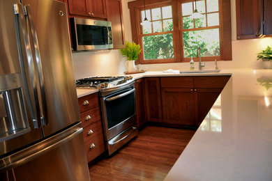 Inspiration for a mid-sized craftsman l-shaped light wood floor and beige floor enclosed kitchen remodel in Indianapolis with an undermount sink, recessed-panel cabinets, medium tone wood cabinets, quartz countertops, white backsplash, stone slab backsplash, stainless steel appliances and no island