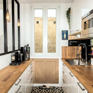 Новые идеи обустройства дома: маленькая параллельная кухня-гостиная в стиле лофт с врезной раковиной, плоскими фасадами, белыми фасадами, столешницей из дерева, черным фартуком, фартуком из сланца, техникой под мебельный фасад и полом из цементной плитки без острова