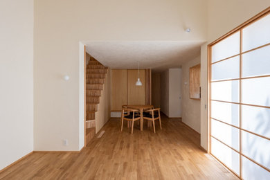 Modelo de salón abierto y beige de tamaño medio con paredes beige, suelo de madera clara, televisor colgado en la pared y suelo beige