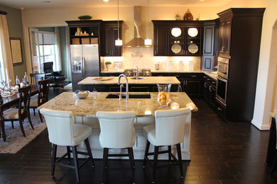 Inspiration for a large timeless l-shaped dark wood floor open concept kitchen remodel in Austin with an undermount sink, raised-panel cabinets, dark wood cabinets, granite countertops, beige backsplash, stainless steel appliances and two islands