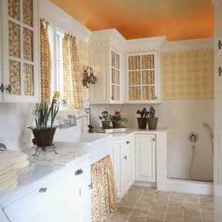 Modelo de lavadero multiusos, clásico, con fregadero sobremueble, armarios tipo vitrina, puertas de armario blancas, encimera de azulejos, paredes amarillas y lavadora y secadora juntas