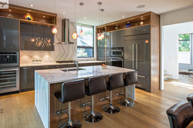 Example of a mid-sized minimalist l-shaped light wood floor and yellow floor open concept kitchen design in Other with an integrated sink, flat-panel cabinets, blue cabinets, granite countertops, white backsplash, granite backsplash, stainless steel appliances, an island and white countertops