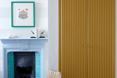 Mittelgroßes Modernes Schlafzimmer mit gelber Wandfarbe, gebeiztem Holzboden, Kamin, Kaminumrandung aus Holz und weißem Boden in London