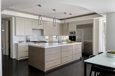 Large trendy u-shaped dark wood floor, brown floor and tray ceiling eat-in kitchen photo in Minneapolis with an undermount sink, flat-panel cabinets, beige cabinets, marble countertops, white backsplash, marble backsplash, stainless steel appliances, an island and white countertops