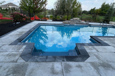 Large minimalist backyard concrete paver and custom-shaped pool landscaping photo in Ottawa