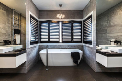 Photo of a large contemporary master bathroom in Brisbane with a vessel sink, flat-panel cabinets, beige cabinets, engineered quartz benchtops, a freestanding tub, a double shower, a wall-mount toilet, porcelain tile and porcelain floors.