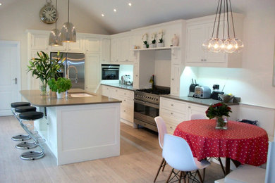 This is an example of a large rural l-shaped kitchen/diner in Sussex with a submerged sink, shaker cabinets, white cabinets, quartz worktops, stainless steel appliances, porcelain flooring, an island, beige floors, beige worktops and a vaulted ceiling.