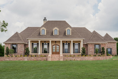 Example of a french country red one-story brick house exterior design in Dallas with a hip roof, a shingle roof and a brown roof