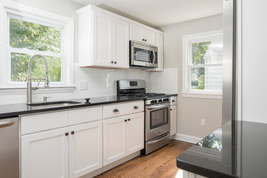 Inspiration for a mid-sized craftsman u-shaped medium tone wood floor and brown floor enclosed kitchen remodel in Bridgeport with an undermount sink, shaker cabinets, white cabinets, solid surface countertops, white backsplash, subway tile backsplash, stainless steel appliances and a peninsula