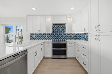 Inspiration for a mid-sized coastal l-shaped light wood floor and beige floor kitchen pantry remodel in Tampa with an undermount sink, shaker cabinets, white cabinets, quartz countertops, blue backsplash, ceramic backsplash, stainless steel appliances, a peninsula and white countertops