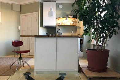 Cette image montre une petite cuisine américaine linéaire et encastrable nordique avec un évier encastré, un placard à porte plane, des portes de placard blanches, un plan de travail en bois, une crédence verte, parquet clair, îlot, un sol beige et un plan de travail beige.