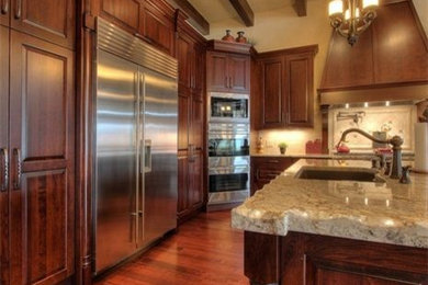 Example of a large classic l-shaped dark wood floor eat-in kitchen design in Other with an undermount sink, raised-panel cabinets, dark wood cabinets, granite countertops, white backsplash, ceramic backsplash, stainless steel appliances and two islands