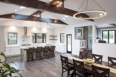 Large arts and crafts l-shaped medium tone wood floor and brown floor eat-in kitchen photo in Los Angeles with a farmhouse sink, shaker cabinets, white cabinets, quartz countertops, white backsplash, glass sheet backsplash, stainless steel appliances and an island
