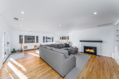 Example of a large minimalist light wood floor and beige floor living room design in Denver with white walls, a standard fireplace and a brick fireplace