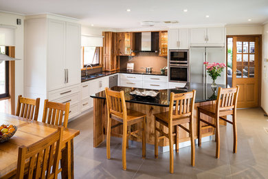 This is an example of a mid-sized modern l-shaped eat-in kitchen in Melbourne with a double-bowl sink, medium wood cabinets, granite benchtops, brown splashback, glass sheet splashback, stainless steel appliances, ceramic floors and with island.