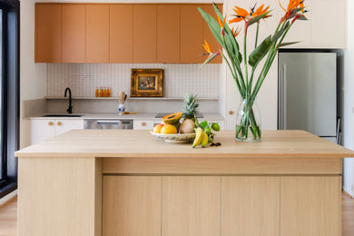 Design ideas for a mid-sized eclectic galley eat-in kitchen in Melbourne with an undermount sink, flat-panel cabinets, pink cabinets, wood benchtops, white splashback, mosaic tile splashback, stainless steel appliances, laminate floors, with island, yellow floor and yellow benchtop.
