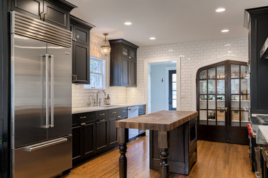 Small transitional medium tone wood floor and brown floor eat-in kitchen photo in Other with a single-bowl sink, recessed-panel cabinets, black cabinets, quartz countertops, white backsplash, porcelain backsplash, stainless steel appliances, an island and white countertops