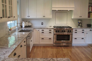 Inspiration for a mid-sized timeless u-shaped light wood floor kitchen remodel in Denver with a farmhouse sink, shaker cabinets, white cabinets, granite countertops, white backsplash and subway tile backsplash