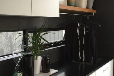 Photo of a mid-sized contemporary single-wall dedicated laundry room in Perth with an undermount sink, white cabinets, quartz benchtops, black walls, porcelain floors and a side-by-side washer and dryer.