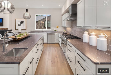Example of a large minimalist l-shaped light wood floor and beige floor open concept kitchen design in Seattle with a single-bowl sink, shaker cabinets, white cabinets, quartz countertops, beige backsplash, glass tile backsplash, stainless steel appliances and an island