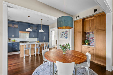 Example of a mid-sized transitional l-shaped medium tone wood floor and brown floor eat-in kitchen design in Chicago with an undermount sink, shaker cabinets, blue cabinets, quartzite countertops, white backsplash, ceramic backsplash, paneled appliances, an island and white countertops