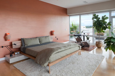 This is an example of a large contemporary master bedroom in New York with orange walls, light hardwood floors, no fireplace and beige floor.