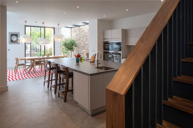 This is an example of a large contemporary single-wall kitchen/diner with an integrated sink, flat-panel cabinets, white cabinets, granite worktops, blue splashback, glass sheet splashback, integrated appliances, porcelain flooring, an island, grey floors, grey worktops and a feature wall.